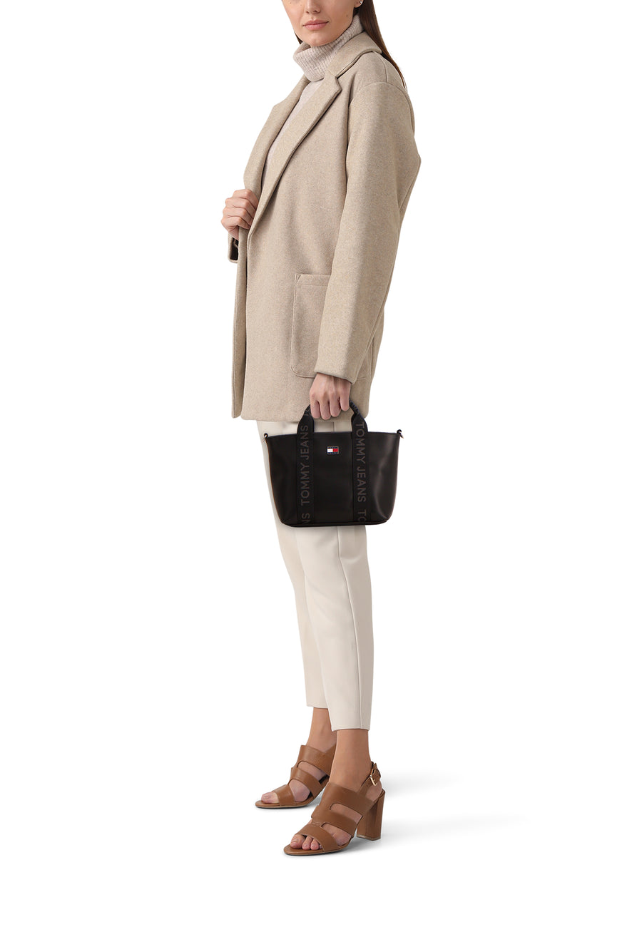 Sac à dos noir de TOMMY JEANS, avec des sangles logo et porté avec une veste beige et un pantalon crème.