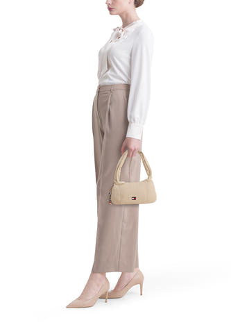 Sac bandoulière beige de TOMMY JEANS, avec des détails argentés et associé à une blouse blanche et un pantalon beige à talons.
