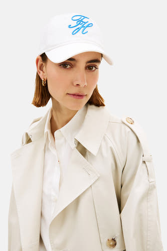 Casquette blanche TOMMY JEANS, avec logo bleu brodé sur le devant, portée avec un trench-coat et une chemise blanche.