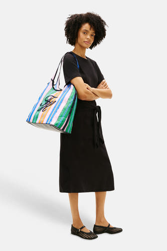 Sac à bandoulière multicolore Tommy Jeans avec motif rayé et détail de logo noir, porté avec une robe noire et des chaussures tressées.