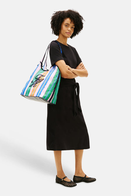 Sac à bandoulière multicolore Tommy Jeans avec motif rayé et détail de logo noir, porté avec une robe noire et des chaussures tressées.