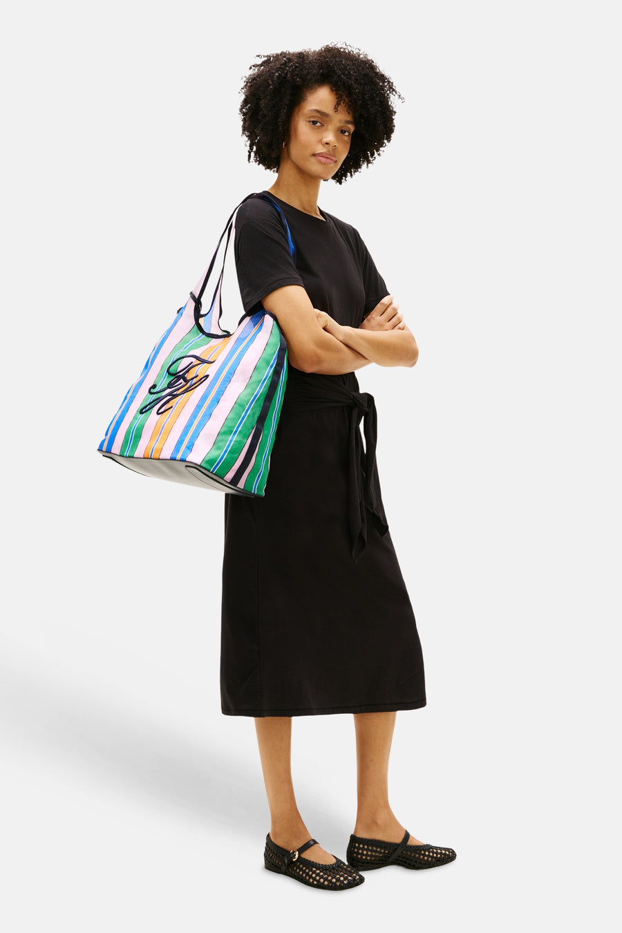 Sac à bandoulière multicolore Tommy Jeans avec motif rayé et détail de logo noir, porté avec une robe noire et des chaussures tressées.