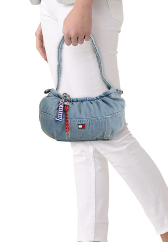 Blauwe denim schoudertas van TOMMY JEANS met ruches, logo-badge en rode touwtjes, gedragen op de heup in lifestyle-opname