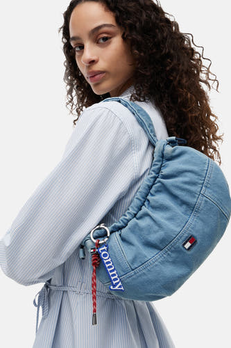 Blauwe denim schoudertas van TOMMY JEANS, met ritsdetails en logo-badge, gedragen over de schouder, lifestyle shot