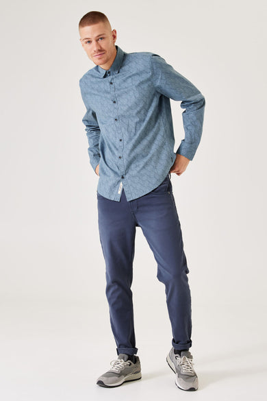 Chemise bleue à manches longues de GARCIA, avec des motifs de vagues subtils, associée à un pantalon bleu marine et des baskets grises.