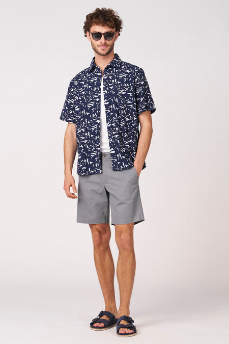 Bermuda bleu de Bruce & Butler, combinée avec une chemise blanche et une chemise ouverte bleu foncé à motifs.