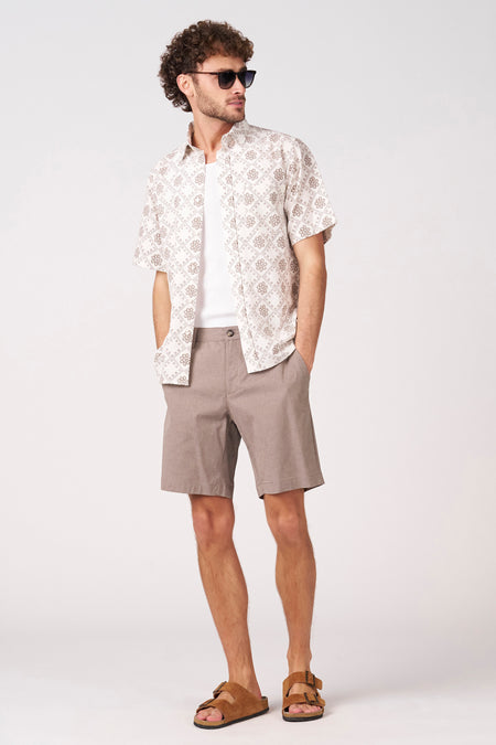 Bermuda beige de Bruce & Butler, avec une texture subtile et une coupe classique, combinée à un t-shirt blanc et des sandales en cuir.