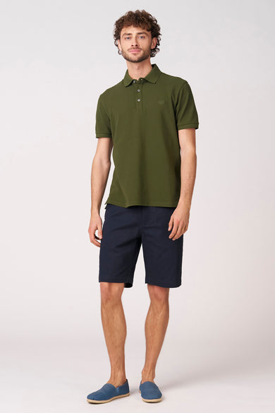 Bermuda bleu de Bruce & Butler, à motif uni et combiné avec un polo vert olive et des espadrilles bleues.