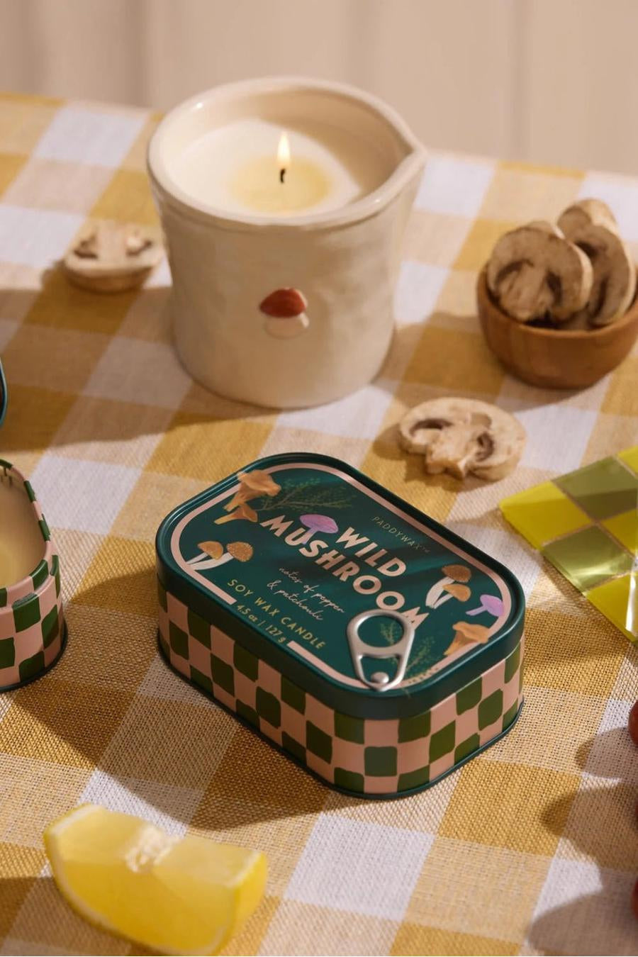 Groene soja-kaars in blik met paddenstoelenprint van PADDY WAX, op geruit tafelkleed met citroen en houten schaaltje