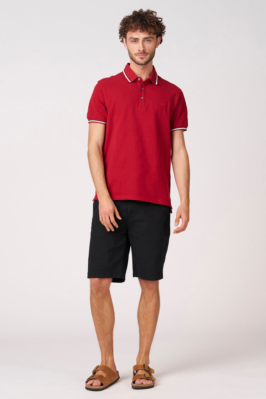 Short noir de Bruce & Butler, combiné avec un polo rouge à détails blancs et des sandales en daim.