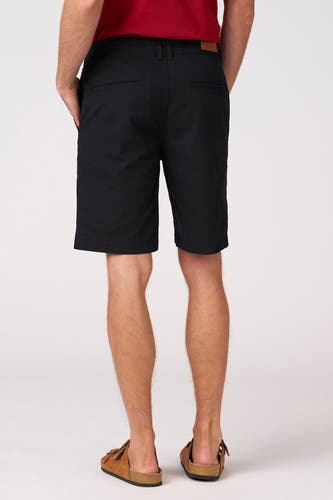 Zwarte bermuda short van Bruce & Butler, met steekzakken en een label op de achterzijde, gedragen met bruine sandalen.
