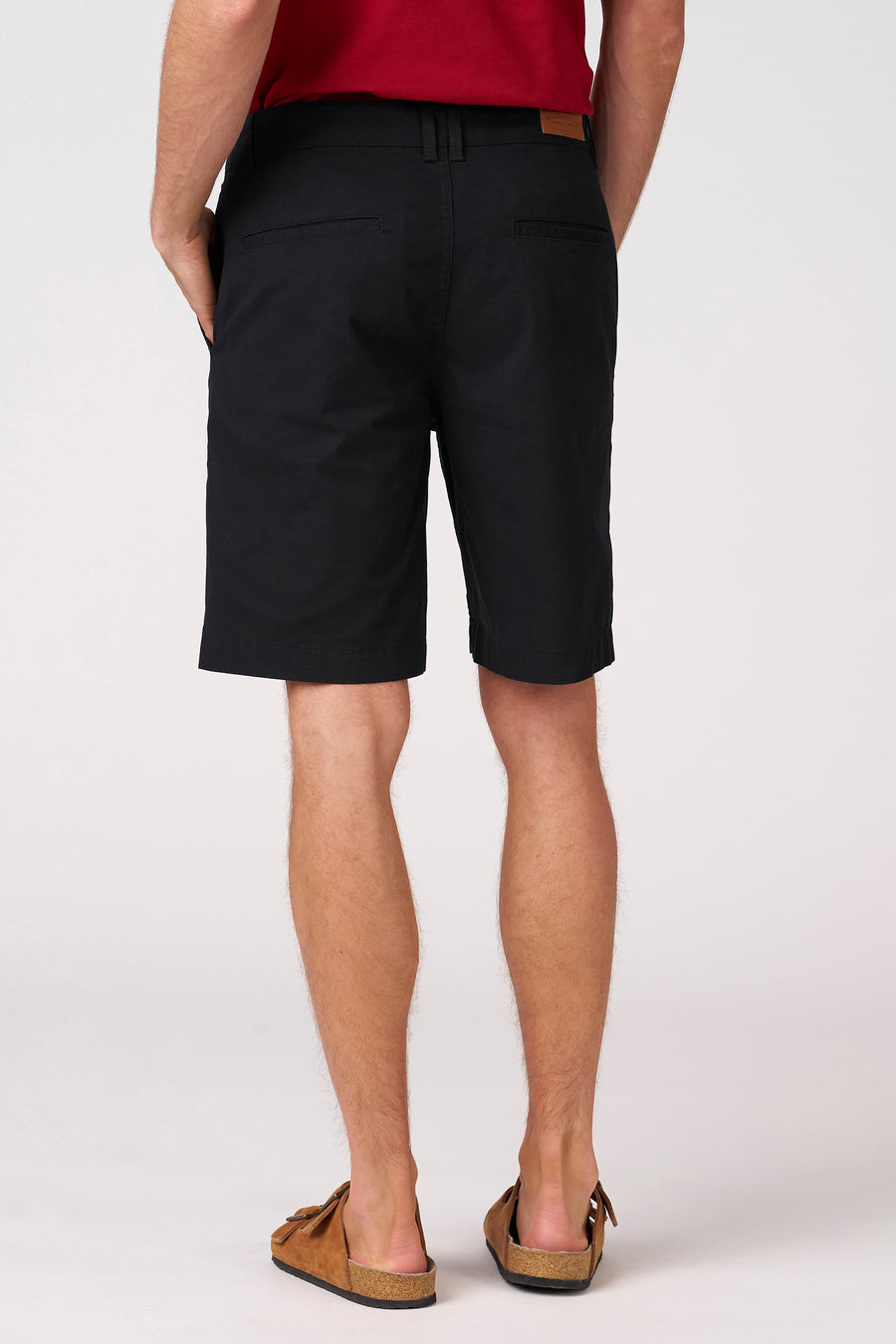 Zwarte bermuda short van Bruce & Butler, met steekzakken en een label op de achterzijde, gedragen met bruine sandalen.
