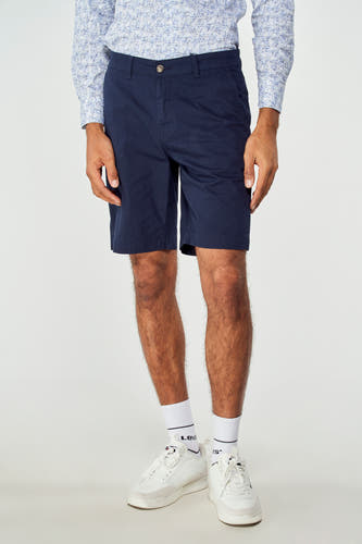 Bermuda bleue de Bruce & Butler, portée avec une chemise imprimée et des baskets blanches avec des chaussettes.