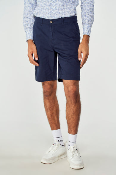 Bermuda bleue de Bruce & Butler, portée avec une chemise imprimée et des baskets blanches avec des chaussettes.