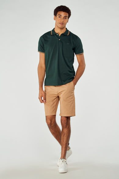 Short de bermuda brune de Bruce & Butler, porté avec une polo verte foncée et des baskets blanches.
