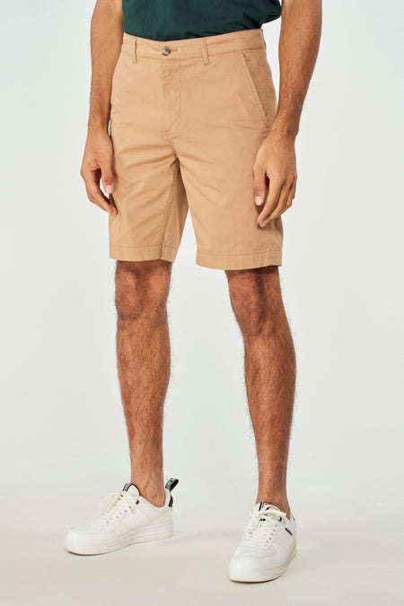 Short brun de Bruce & Butler, avec un dessin lisse, porté avec un t-shirt vert et des baskets blanches.