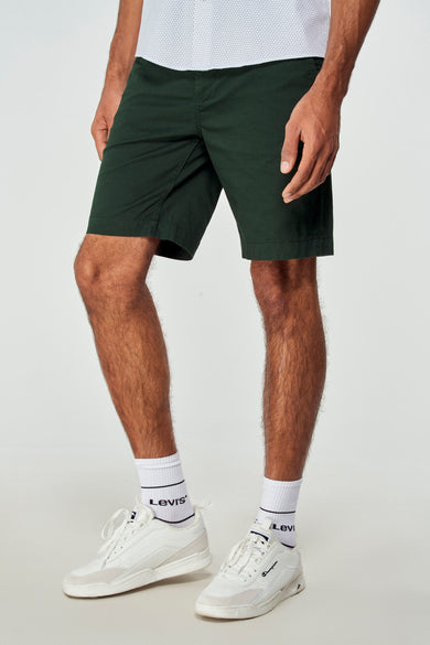 Short bermuda vert de Bruce & Butler, coupe ajustée, modèle portant un t-shirt en mesh blanc et des baskets blanches, vue de face