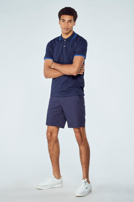 Short bermuda bleu de Bruce & Butler, détails de col rayés, modèle en pied avec baskets blanches