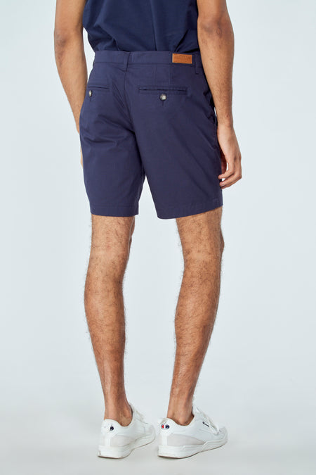 Short bermuda bleu de Bruce & Butler, dos avec deux poches et étiquette marron, le modèle porte des baskets blanches