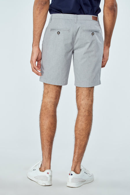Short bleu de Bruce & Butler, vue arrière avec poches à boutons, porté avec des chaussures blanches.