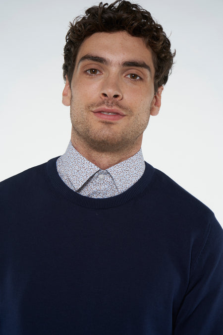 T-shirt bleu avec col rond de Bruce & Butler, porté sous une chemise à fleurs.