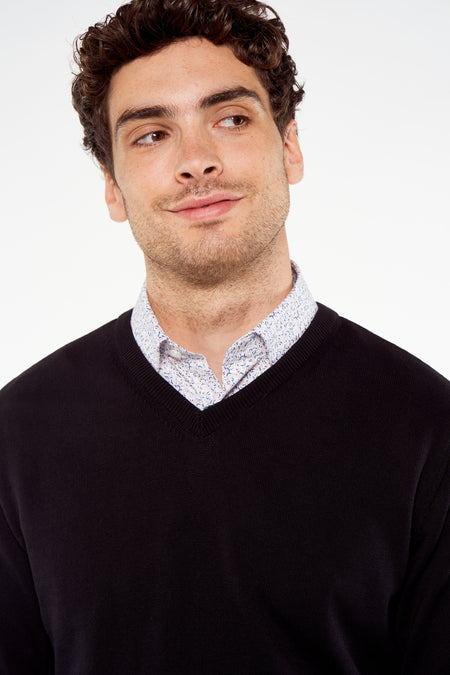 Pull à col en V noir de Bruce & Butler, tricoté avec une texture fine, porté sur une chemise rayée, gros plan sur l'avant.