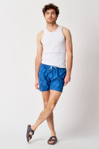 Maillot de bain bleu de Bruce & Butler, avec motif végétal, associé à un t-shirt blanc et des sandales.
