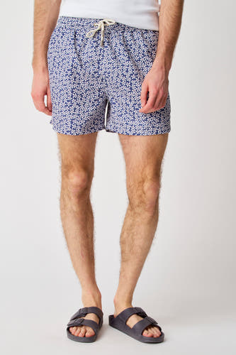 Maillot de bain bleu de Bruce & Butler avec imprimé fleuri, porté avec des sandales et une chemise blanche.