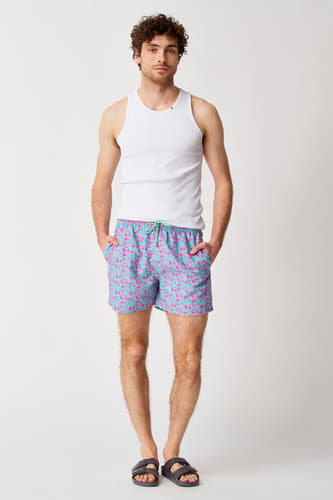 Maillot de bain bleu de Bruce & Butler, avec un motif de fleurs roses, porté avec une chemise blanche et des sandales grises.