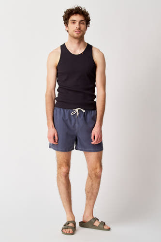Jean bleu de Bruce & Butler, porté avec un tank-top noir et des sandales vertes.