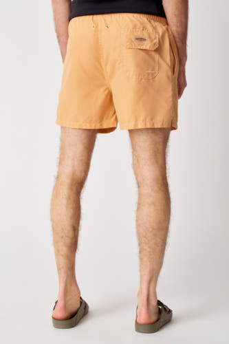 Pantalon de bain Bruce & Butler, avec poche à l'arrière et porté avec des sandales.