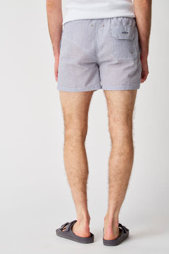Pantalon bleu de Bruce & Butler en un motif seersucker à rayures, vu de derrière, porté avec des sandales.