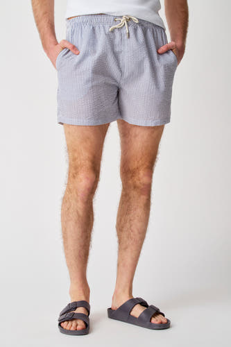 Pantalon de bain bleu de Bruce & Butler avec des rayures verticales et une corde, porté avec des sandales.