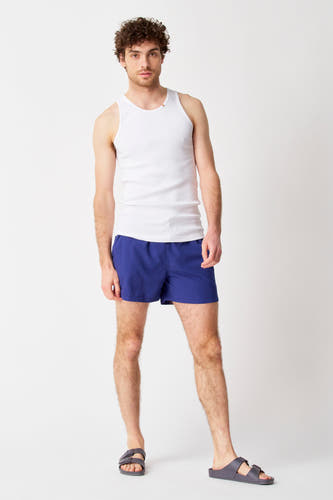 Pantalon de bain bleu Bruce & Butler, porté avec une chemise blanche et des sandales grises.