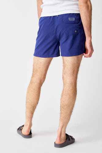 Pantalon de bain bleu de Bruce & Butler, vu de derrière, avec une poche arrière et porté avec des sandales.
