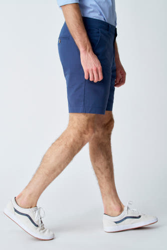 Blauwe short van Bruce & Butler, gezien van de zijkant, gecombineerd met een lichtblauw overhemd en witte sneakers.
