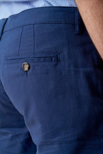 Blauwe short van Bruce & Butler met een bruine knoop op de achterzak, in een cropped close-up.
