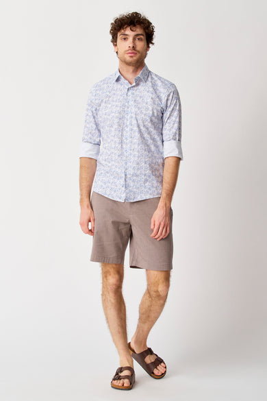 Man in overhemd met print, bruine shorts en sandalen.