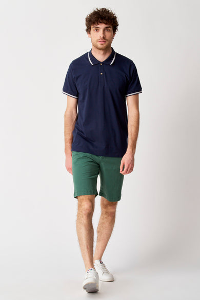 Short vert de Bruce & Butler, porté avec un poloshirt bleu foncé à détails blancs et des baskets blanches.