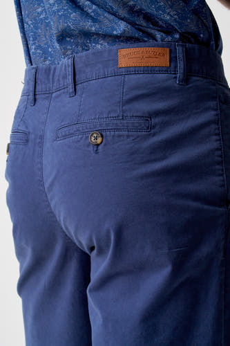 Short bleu de Bruce & Butler, avec poche arrière et bouton marron, porté avec un chemisier à fleurs bleues.