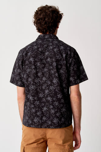 Chemise noire à manches courtes de Bruce & Butler avec motif à feuilles, dos, combinée avec un short cargo de couleur camel.