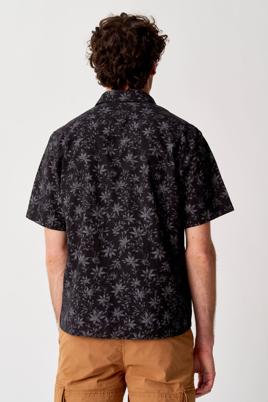 Chemise noire à manches courtes de Bruce & Butler avec motif à feuilles, dos, combinée avec un short cargo de couleur camel.