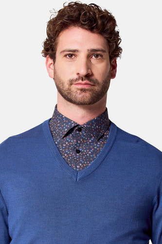 Pull-over V-hals bleu de Bruce & Butler, avec une texture fine et soyeuse, porté sur un chemisier à imprimé floral.
