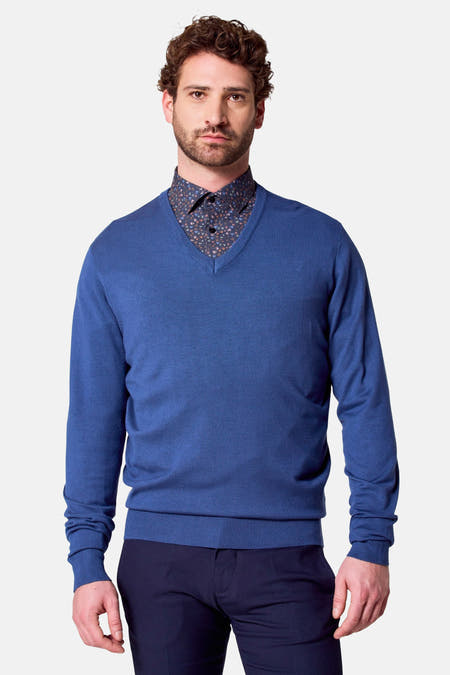 Pull à col V bleu de Bruce & Butler, porté sur une chemise imprimée, avec des manches longues et un pantalon foncé.