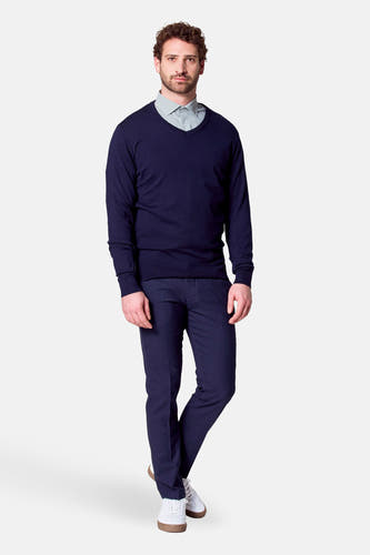 Pull à col V bleu de Bruce & Butler, porté sur une chemise et avec un pantalon foncé et des baskets blanches.