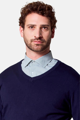 Pull à col V bleu de Bruce & Butler, porté sur une chemise à motif.