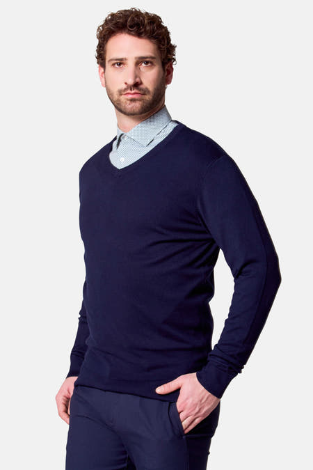 T-shirt à col V bleu de Bruce & Butler, avec un chemisier rayé bleu clair en dessous, debout.
