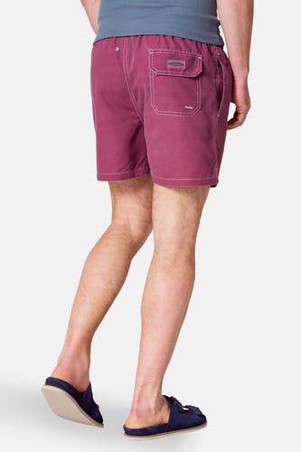 Maillot de bain Bordeaux de Bruce & Butler, avec des coutures blanches et une poche arrière, porté avec des sandales bleues.