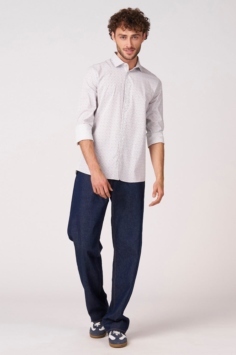 Chemise blanche (manches longues) de Bruce & Butler, avec un motif subtil et portée avec un jean foncé et des baskets.