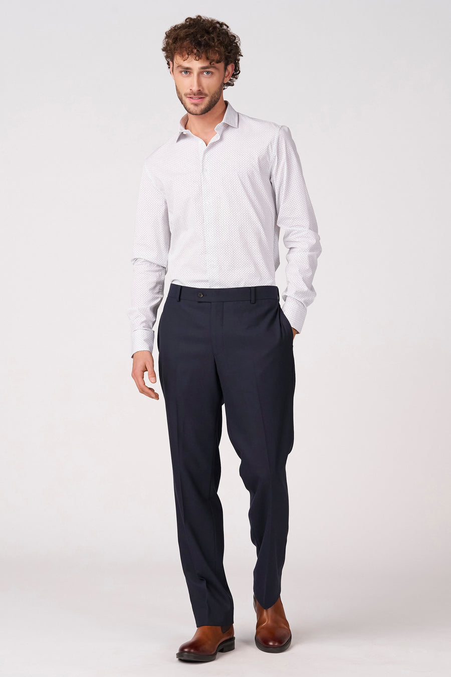 Chemise blanche à manches longues de Bruce & Butler, ornée d'un subtil motif à pois et portée avec un pantalon bleu foncé et des chaussures marron.